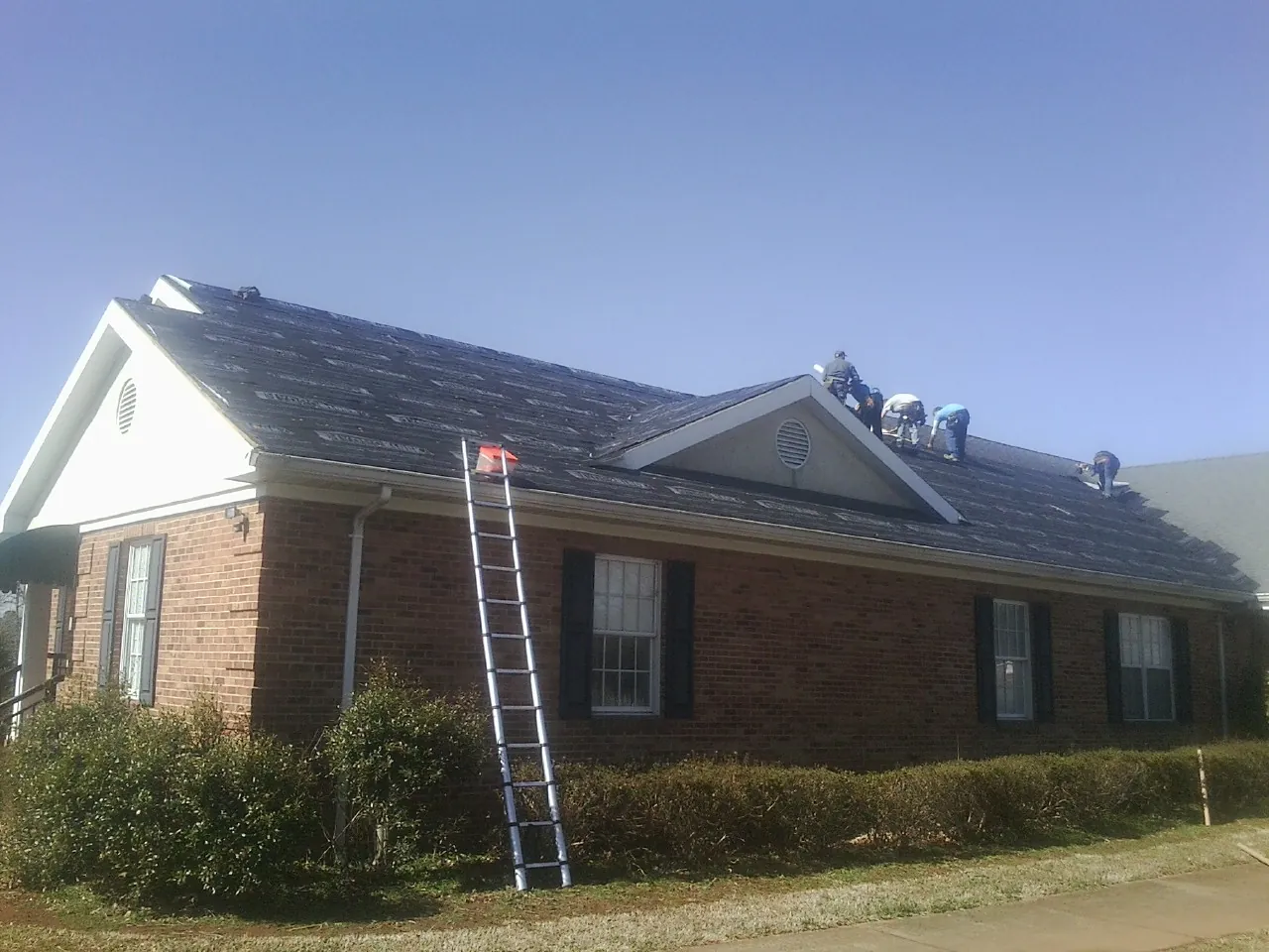 Crew tearing shingles off a brick ranch roof with a ladder set — Metal Roof Repair work by our crew in East Walpole