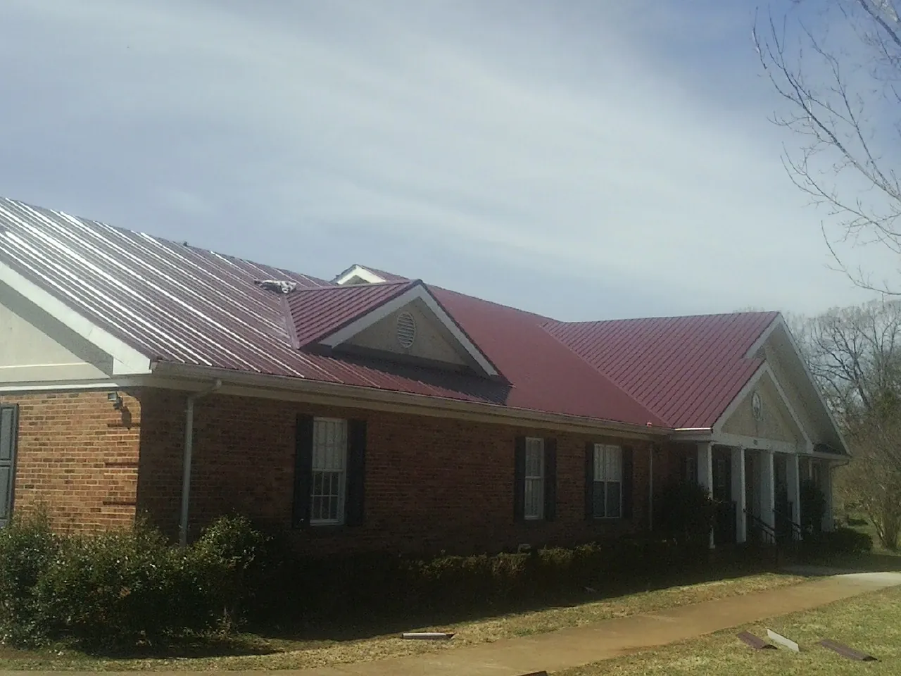 Red metal roof with gabled entries on a long brick building, from a Hail Damage Roof Repair job in East Walpole