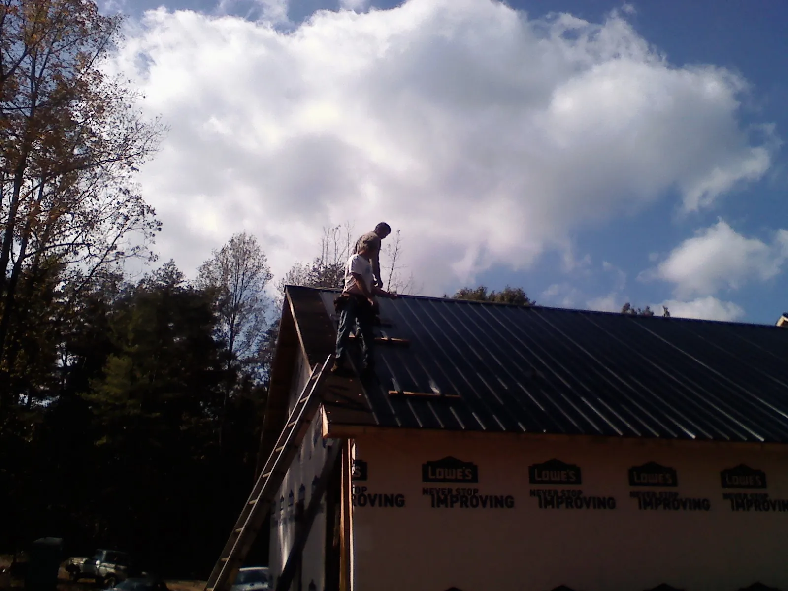 Roofer fastening dark metal panels high against a cloudy sky, from a Roof Inspection job in East Walpole