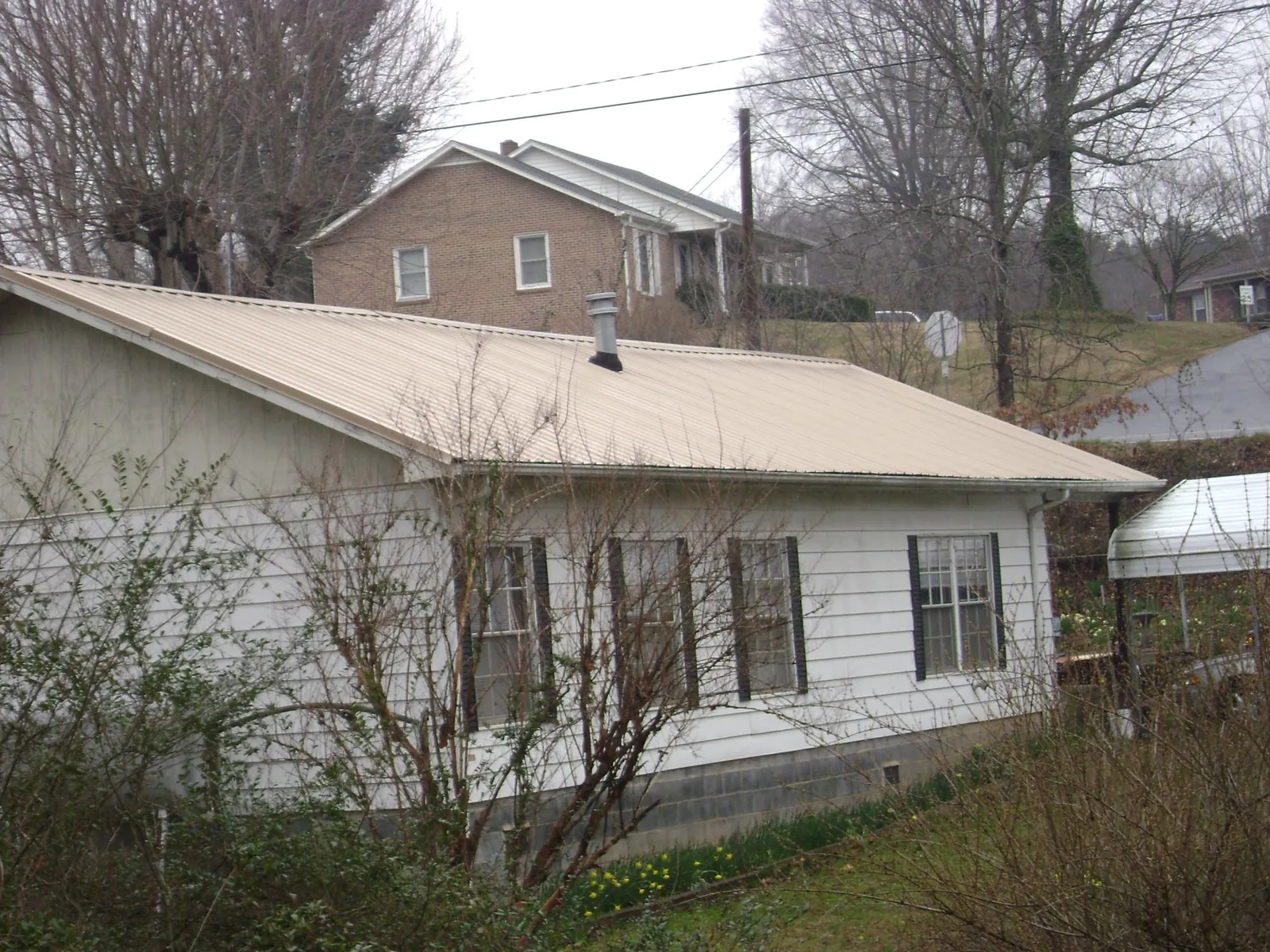 Tan metal roof on a white sided house set into a hillside — Commercial Roofing by Roofing Brothers in East Walpole