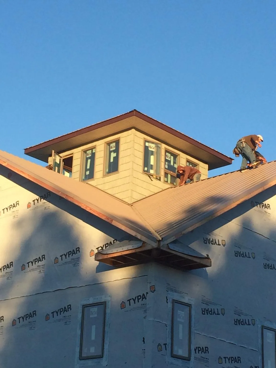 Roofers working around a rooftop cupola on a new metal roof at sunset in East Walpole